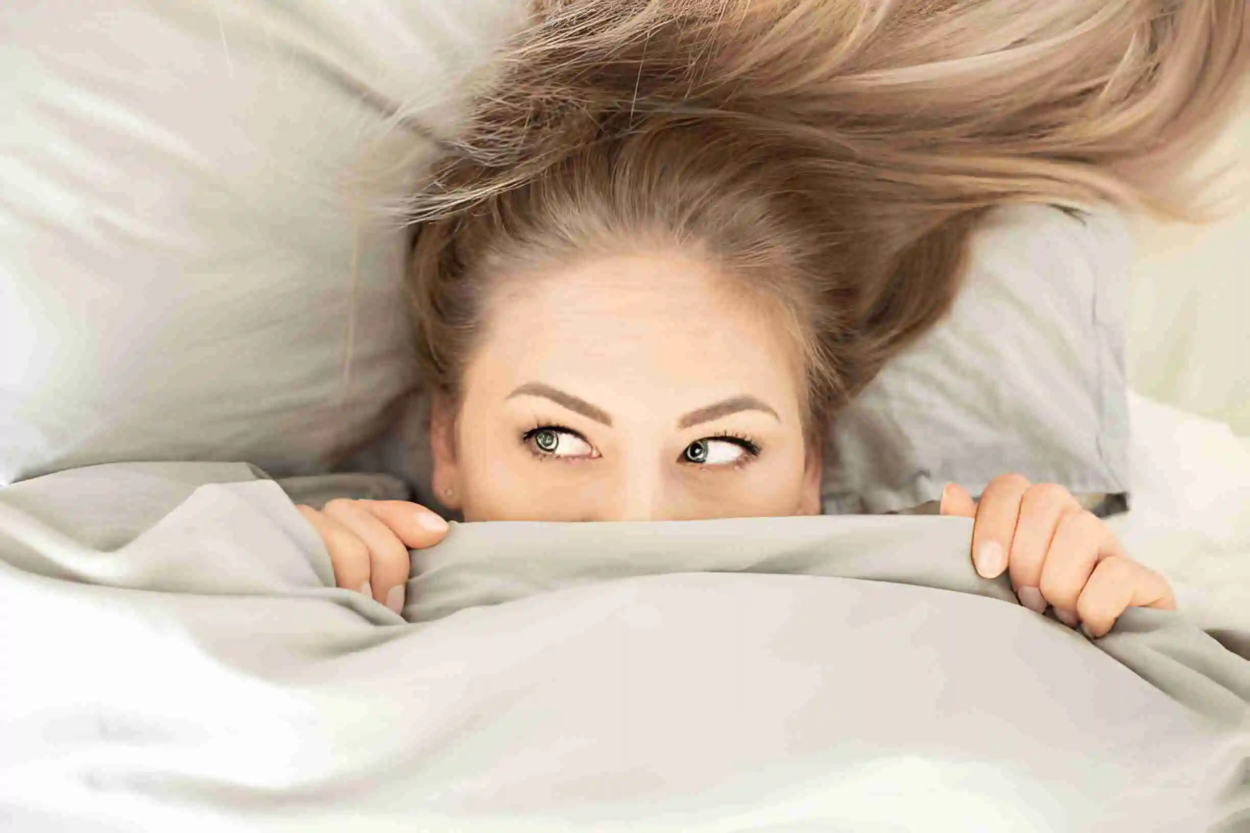 Young woman peeking out from under duvet, playful expression